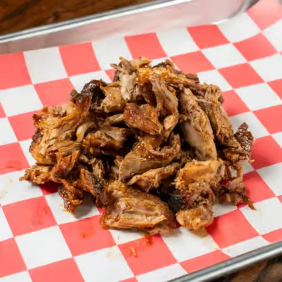 Pile of shredded, saucy BBQ meat on red and white checkered paper in a metal tray.