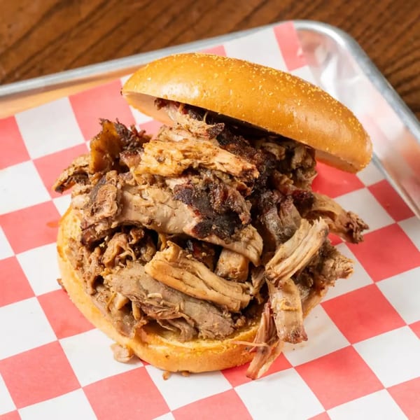Close-up of a pulled pork sandwich on a sesame seed bun, served on red and white checkered paper.