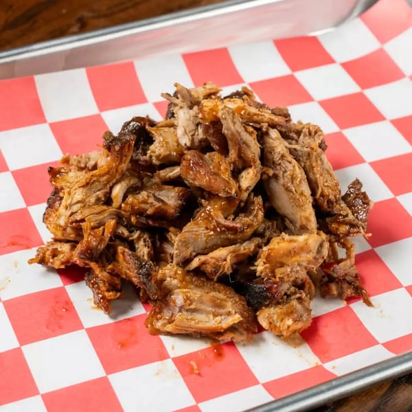 A mound of juicy, shredded barbecue pork on red and white checkered paper.
