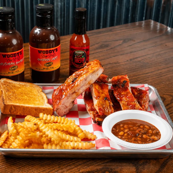 Woody's Bar-B-Q ribs, fries, toast, and baked beans, with three sauce bottles on a tray.